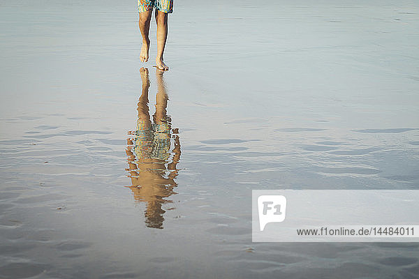 Jugendlicher  der am nassen Sandstrand spazieren geht