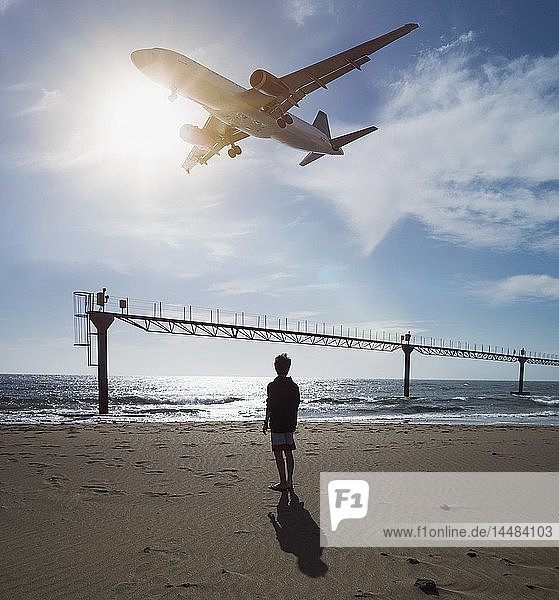 Junge blickt auf ein Flugzeug  das im Tiefflug über den Ozean in der Nähe des Flughafens von Lanzarote  Puerto del Carmen  Spanien  fliegt