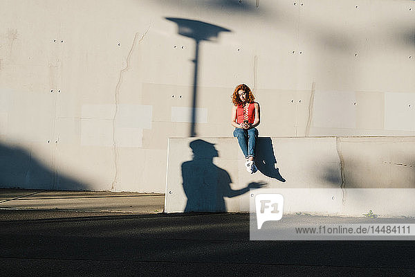 Schatten  der zu einer jungen Frau aufblickt  die ein Smartphone an einer Hauswand benutzt
