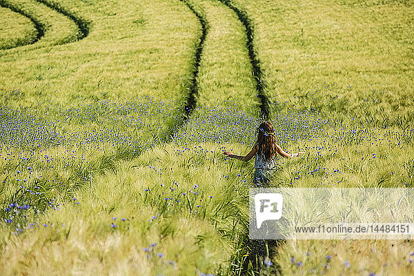 Unbekümmertes Mädchen  das in einem sonnigen  idyllischen Feld mit Wildblumen spazieren geht