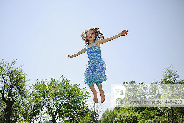 Unbekümmertes Mädchen im Kleid springt vor Freude im sonnigen Hinterhof