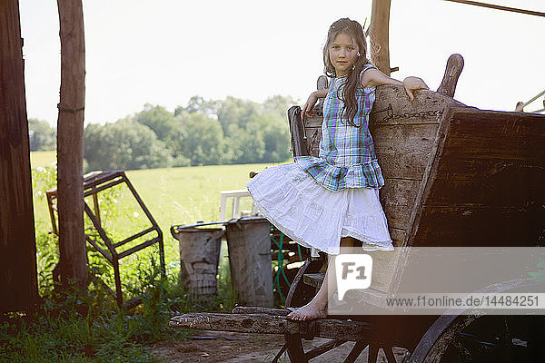 Porträt barfüßiges Mädchen im Kleid  das sich an einen ländlichen Wagen lehnt