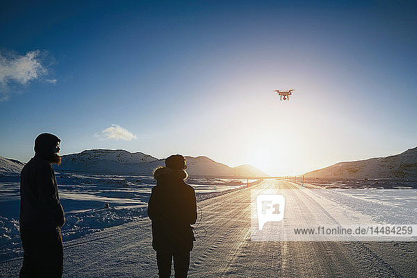 Vater und Sohn fliegen Drohne über abgelegene  schneebedeckte Straße  Reykjadalur  Island