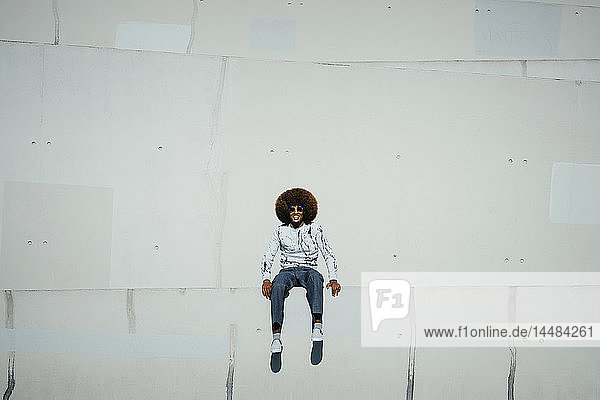 Porträt glücklicher junger Mann mit Afro an der Wand sitzend