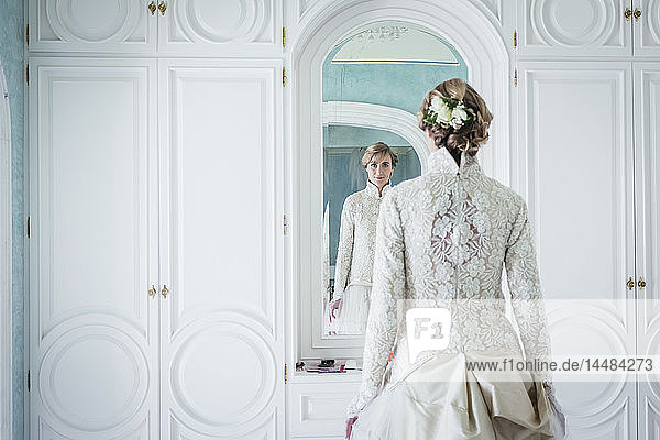 Elegante Braut im Spitzenhochzeitskleid am Spiegel