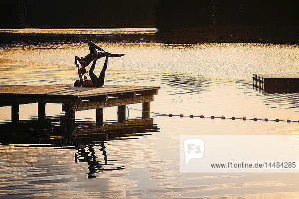 Frauen üben Acro-Yoga auf einem Dock am See in der Abenddämmerung