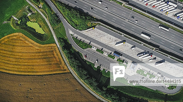 Drohnensicht auf Sattelschlepper  die auf einem Rastplatz zwischen Autobahn und Ackerland geparkt sind  Bayern  Deutschland