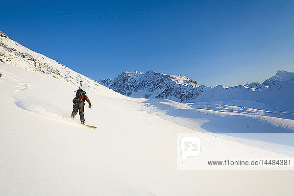 Ein Mann fährt mit dem Snowboard einen Berg in der Nähe von Eagle River hinunter. Winter in Süd-Zentral-Alaska.