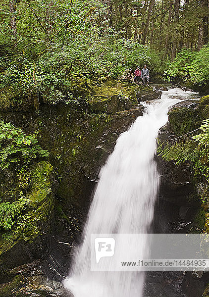 Two hikers stand at the top of Sawmill Creek Falls in the Tongass National Rainforest near Juneau  Southeast Alaska
