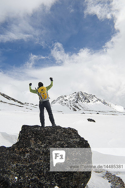Eine Wanderin steht auf einem großen Felsvorsprung und genießt die Aussicht in den Chugach Mountains in der Nähe des Powerline Pass und des Glen Alps Trailhead  Southcentral  Alaska