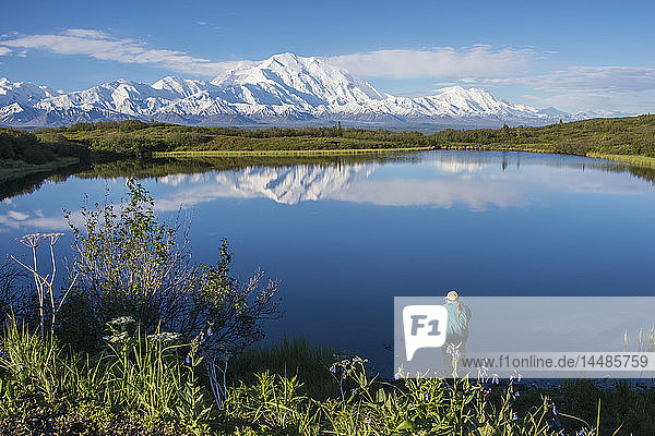 Frau steht am Rande des Reflection Pond und genießt die Aussicht auf den Mt. McKinley und die Alaska Range  Denali National Park  Interior Alaska  Frühling