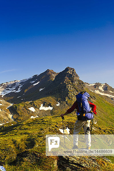 A man backpacking near Hatcher Pass in the Talkeetna Mountains with Bald Mountain Ridge in the background  Southcentral Alaska  Summer