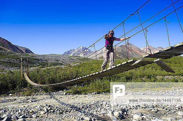 Eine Frau geht auf einer Hängebrücke über den College Creek zum Gulkana-Gletscher  Southcentral Alaska  Sommer/n
