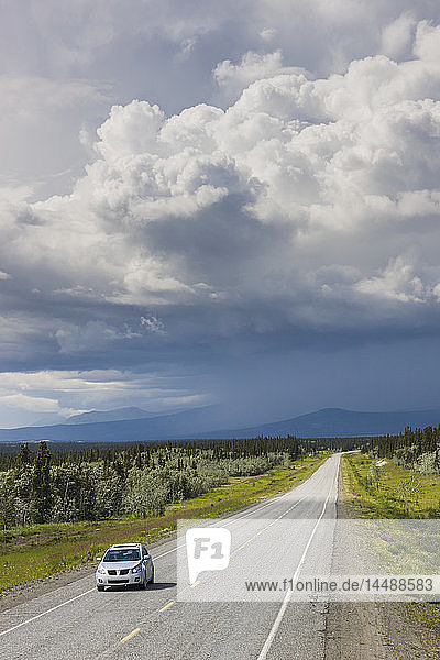 Car driving on the Alaska Highway with stormy clouds overhead  west of Whitehorse  Yukon Territory  Canada  Summer