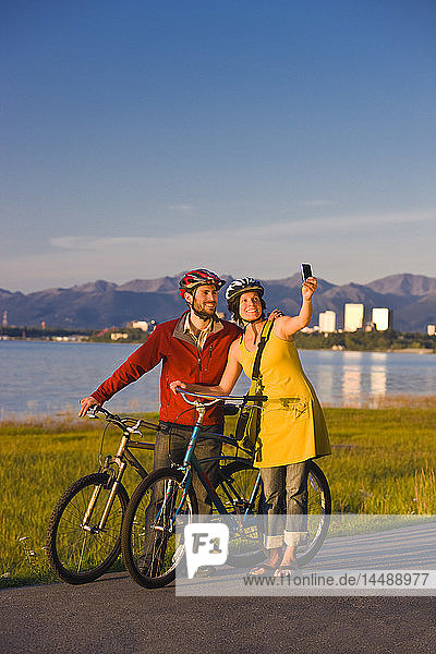 Bicyclists resting and taking self-portraits along the Tony Knowles Coastal Trail with the Anchorage skyline in the background  Southcentral Alaska