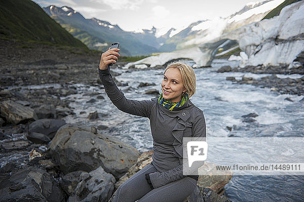 Frau macht mit ihrem Smartphone ein Selfie vor dem Portage Creek  Portage Valley  Southcentral Alaska