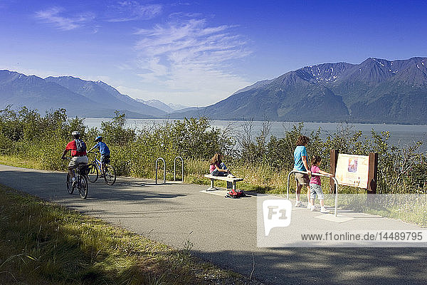 Eine Familie liest ein Informationsschild am Coastal Trail in der Nähe von Indian  AK  während Radfahrer vorbeifahren. SC Alaska Sommer.