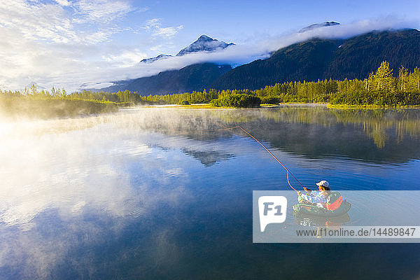Woman in float tube flyfishing on Moose Ponds in Portage Valley Chugach National Forest during Autumn in Southcentral Alaska