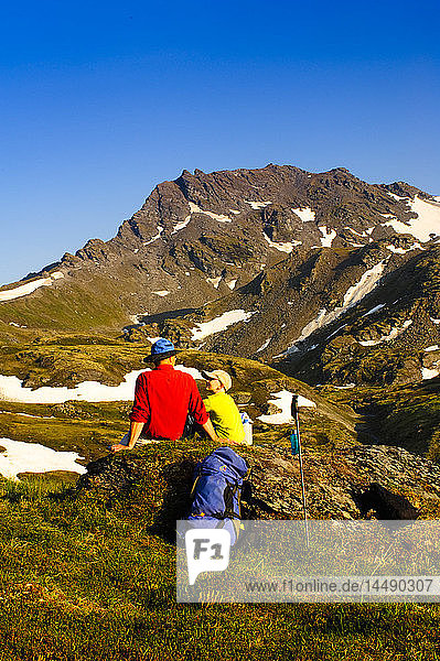 A father and son backpacking near Hatcher Pass in the Talkeetna Mountains with Bald Mountain Ridge in the background  Southcentral Alaska  Summer
