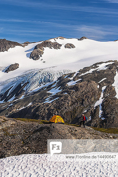 Ein Rucksacktourist auf seinem Campingplatz,  der auf einer Bergkuppe inmitten der zerklüfteten Berge des Kenai Fjords National Park in Süd-Zentral-Alaska liegt.