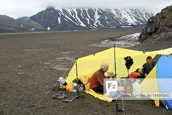 Ein Paar isst unter einer Plane in einem Lager in der Nähe des Surprise Lake im Aniakchak National Monument and Preserve im Südwesten Alaskas