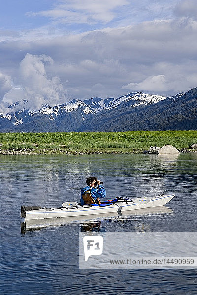 Woman views scenery through binoculars from sea kayak Holkham Bay Tracy Arm Southeast Alaska Summer