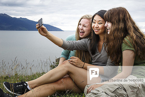 Three multicultural young women taking a group selfie while on a hike along the Turnagain Arm  Southcentral Alaska  Summer