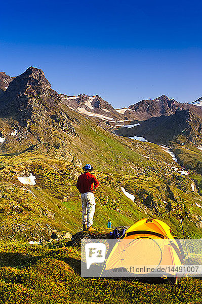 A man at his campsite in the Talkeetna Mountains with Bald Mountain Ridge in the background  Southcentral Alaska  Summer