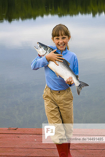 Young girl holding and posing with a Coho salmon at a lake in Anchorage during Summer in Southcentral Alaska
