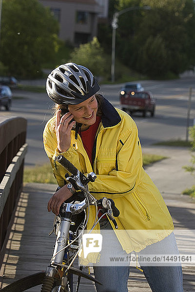 Junges Mädchen spricht mit dem Handy  während sie mit dem Fahrrad unterwegs ist Anchorage Alaska Sommer