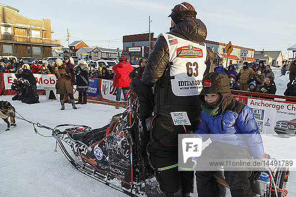 Aaron Burmeister´s Sohn fährt auf dem Schlittenwagen  während Aaron sein Team zum Hundeplatz führt  nachdem er beim Iditarod 2015 den dritten Platz belegt hat