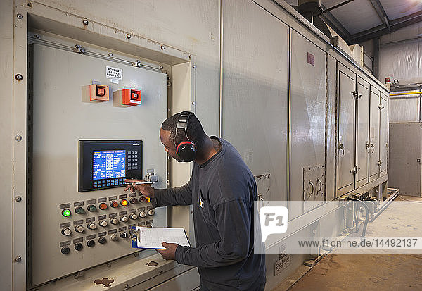 A Male laborer wearing ear protection inspects an electrical power plant control panel  Prudhoe Bay  Arctic Alaska  USA  Summer
