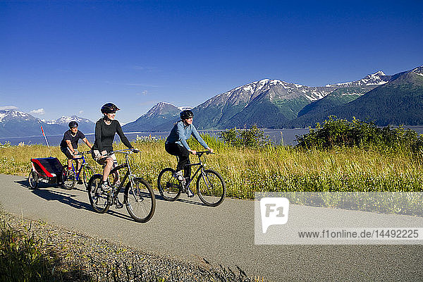 Two women and a man biking on the Bird Point to Girdwood bike trail with a baby stroller during Summer along Turnagain Arm in Southcentral Alaska