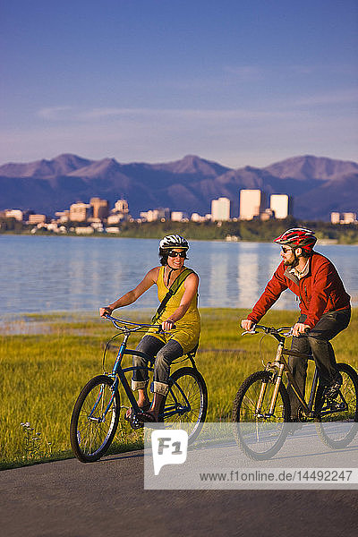 Bicyclists riding on the Tony Knowles Coastal Trail with the Anchorage skyline in the background  Southcentral Alaska
