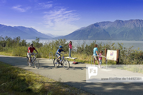 Eine Familie liest ein Informationsschild am Coastal Trail in der Nähe von Indian  AK  während Radfahrer vorbeifahren. SC Alaska Sommer.