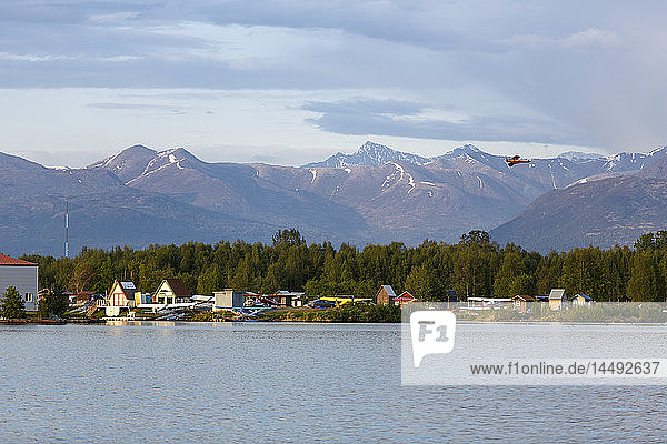 Super Cub airplane flies over Lake Hood with Chugach Mountains in the background  Anchorage  Southcentral Alaska  Summer