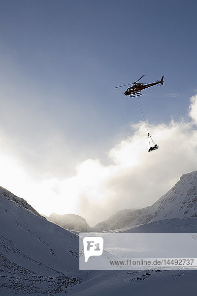 Helicopter carrying sledge near snowcapped mountain