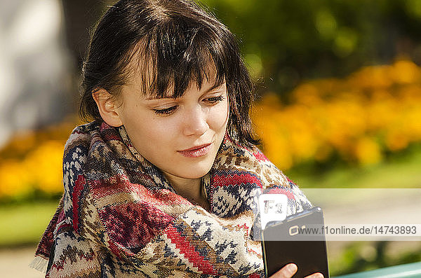 Junge Frau benutzt ein Smartphone in einem Park.