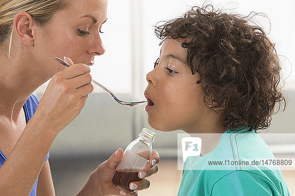 Mother giving her son a spoon of medicine.