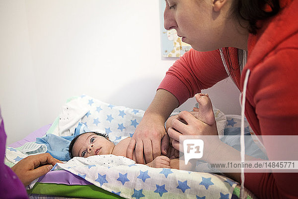Reportage über eine unabhängige Hebamme bei Hausbesuchen nach der Geburt. Die Hebamme tastet den Unterleib des Babys ab.
