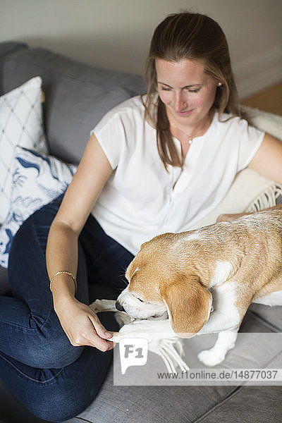 Frau sitzt mit Hund auf dem Sofa