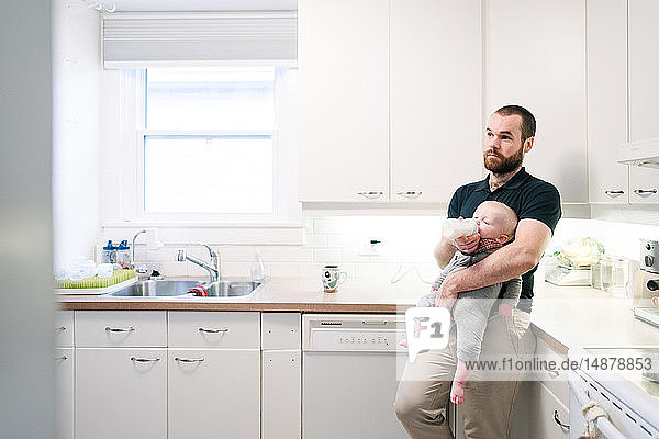 Father bottle feeding baby son in kitchen