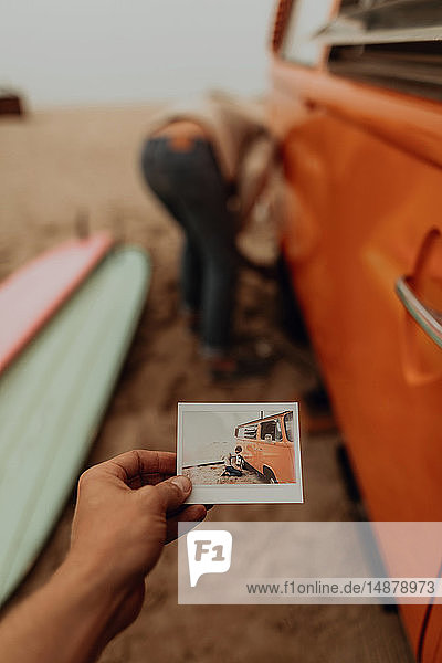 Junge Frau hält ein Sofortfoto von ihrem Freund,  der einen platten Reifen an einem Wohnmobil am Strand entfernt,  Jalama,  Kalifornien,  USA