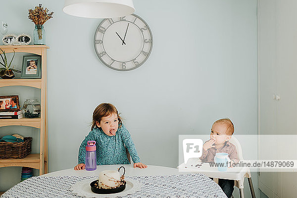 Weibliches Kleinkind am Tisch und kleiner Bruder im Hochstuhl