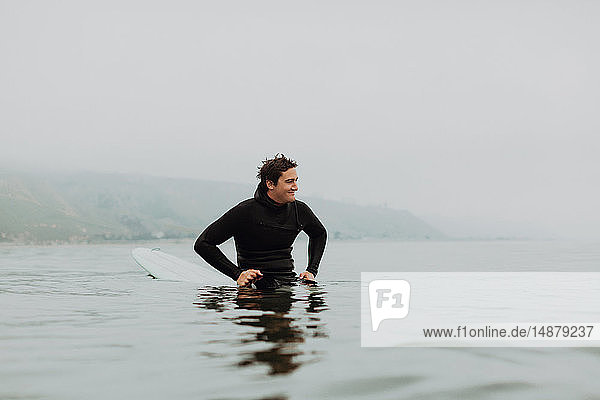 Junger männlicher Surfer sitzt auf einem Surfbrett in ruhiger  nebliger See  Ventura  Kalifornien  USA