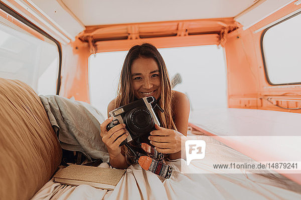 Junge Frau mit Sofortbildkamera auf dem Rücksitz eines Wohnmobils am Strand  Porträt  Jalama  Kalifornien  USA