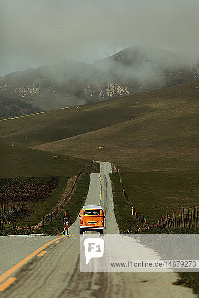 Young woman walking toward recreational vehicle on rural road  Jalama  California  USA