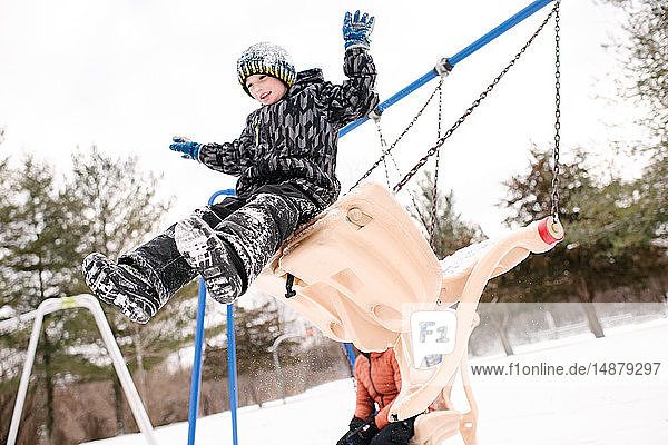 Boy jumping from playground swing in snow