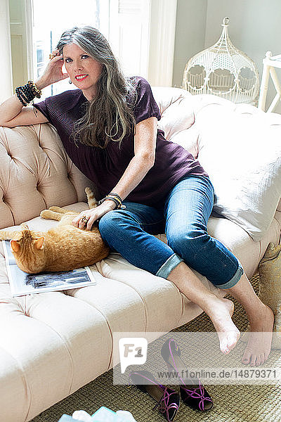 Stylish mature woman sitting on sofa petting ginger cat  portrait