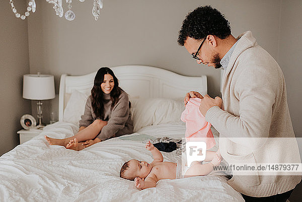 Couple dressing baby daughter on bed in bedroom